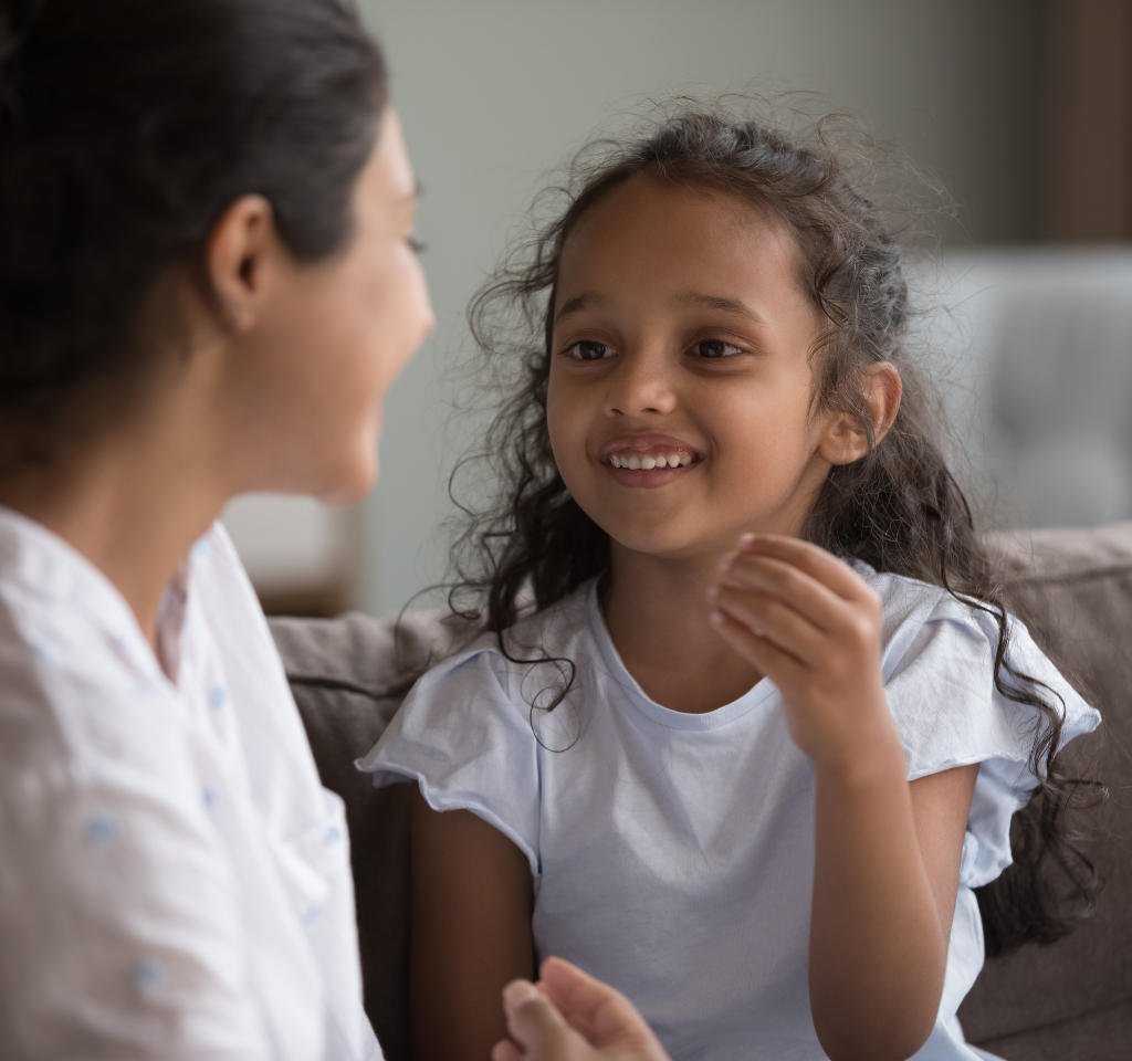 A young girl smiles as she speaks to her speech pathologist.