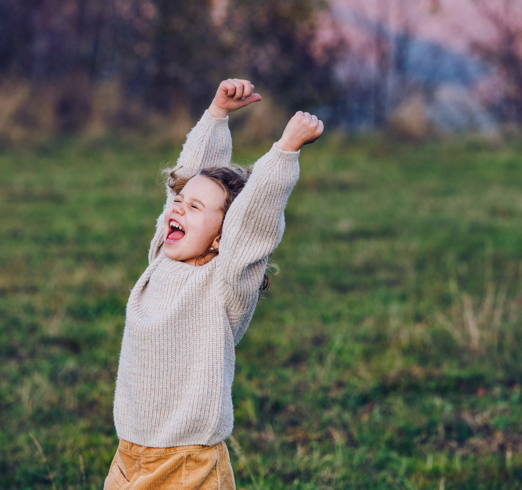 A young girl yells excitedly in a field.